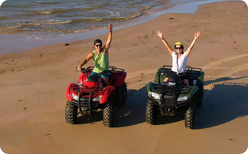 Pessoas se divertindo em passeio de quadriciclo na praia.