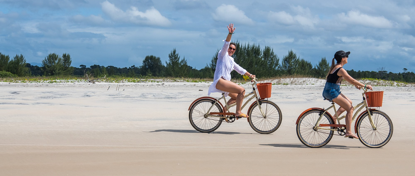 Pessoas andando de bicicleta na praia em dia ensolarado.